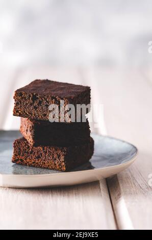 Brownie in un piatto blu chiaro su uno sfondo di legno bianco. Foto Stock