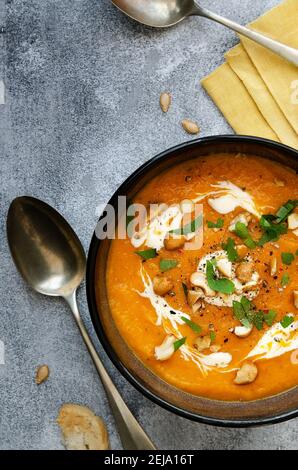 Zuppa di zucca con panna, anacardi e prezzemolo, in una ciotola nera su un piatto di legno. Foto Stock