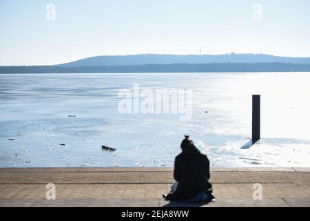 Berlino, Germania. 22 Feb 2021. Una persona è seduta al sole sulla riva del Müggelsee, la cui superficie è ancora un po' congelata. Credit: Kira Hofmann/dpa-Zentralbild/dpa/Alamy Live News Foto Stock