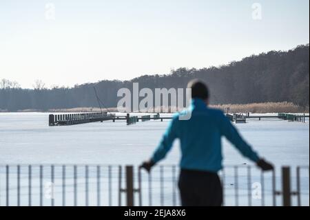 Berlino, Germania. 22 Feb 2021. Una persona è in piedi al sole sulla riva del Müggelsee, la cui superficie è ancora un po' congelata. Credit: Kira Hofmann/dpa-Zentralbild/dpa/Alamy Live News Foto Stock