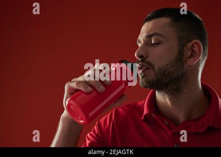 Primo piano in vista laterale ritratto di sportivo forte in abbigliamento sportivo acqua potabile dalla bottiglia con gli occhi vicini Foto Stock