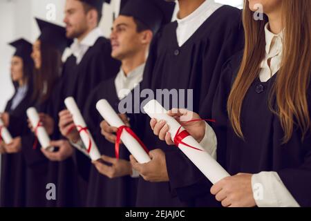 Fila di laureati in cappelli e abiti neri con diplomi alla cerimonia di laurea Foto Stock