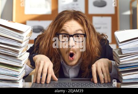 Divertente contabile nerdy seduto alla scrivania dell'ufficio con espressione di sorpresa in faccia Foto Stock