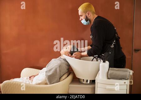 Professionista coiffeur shampooing i capelli sorridenti del cliente Foto Stock