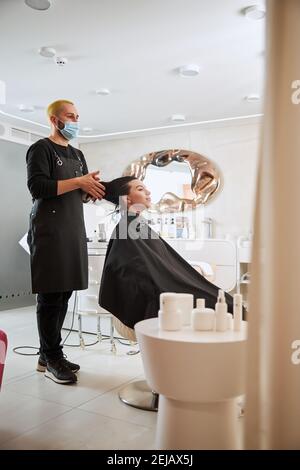 Il coiffeur serio che applica un prodotto di acconciatura sul cuoio capelluto del cliente Foto Stock