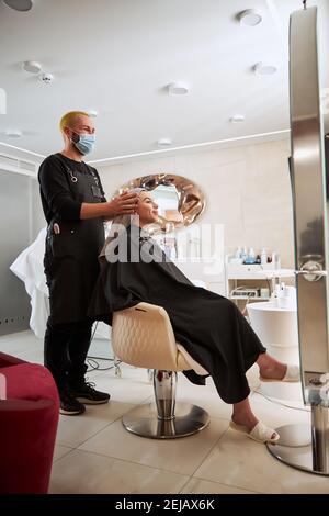 Asciugamano professionale coiffeur-asciugando i capelli del suo giovane cliente Foto Stock