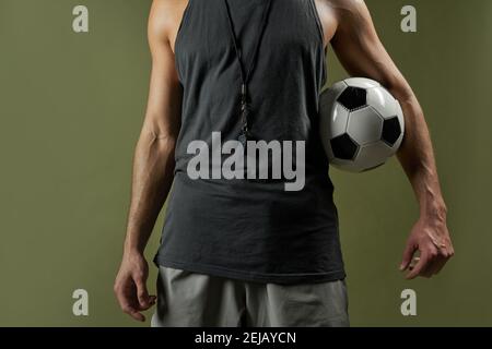 Ritratto a testa tronca di un forte giocatore di calcio non riconosciuto che indossa il colore grigio sportswear tenendo la palla in mano isolato su sfondo verde Foto Stock