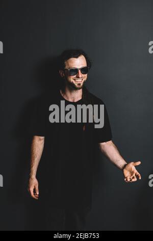 Felice giovane in occhiali da sole in piedi su uno sfondo nero. Ritratto casual. Foto Stock
