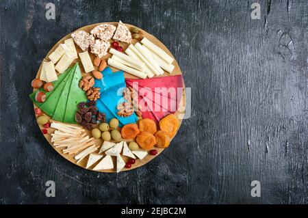 Diversi tipi di formaggi, albicocche secche, pani a grani interi, noci, olive, capperi su una tavola di legno. Formaggio a tavola, spuntini. Spazio di copia. Vista dall'alto Foto Stock