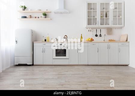 Interno di elegante cucina con pareti chiare, mobili bianchi con utensili e frutta Foto Stock