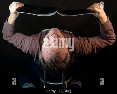 Un uomo di mezza età legge un libro con la testa capovolta giù con un'espressione spiritosa Foto Stock