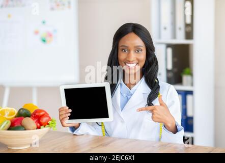 Sito web o applicazione clinica di perdita di peso. Dietician felice nero che punta al Tablet pc con schermo vuoto, mockup Foto Stock