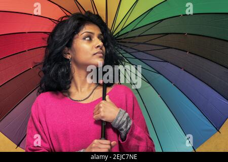 Bella ragazza Sri Lanka posa in piedi con sfondo giallo luminoso Appeso un ombrello colorato - la giovane donna sorride Foto Stock