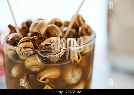 primo piano di un bicchiere con caracolillos spagnolo en caldo, una ricetta di piccole lumache cucinate e servite in brodo tipico dell'andalusia, su un tavolo Foto Stock