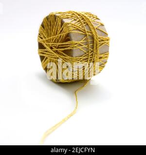 Bobina in filo giallo con avvolgimento intricato su sfondo bianco che mostra materiali tessili e oggetti essenziali per la lavorazione Foto Stock