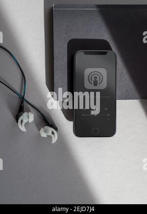 Telefono nero con un podcast in riproduzione e un notebook e auricolari accanto. Foto Stock