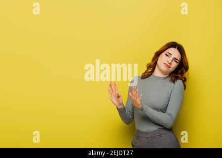 donna disgustata che mostra il gesto di stop mentre si guarda via sul giallo Foto Stock