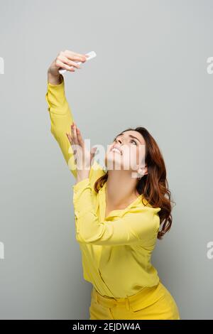 donne che si piegano gesturing mentre prendendo selfie su smartphone su grigio Foto Stock