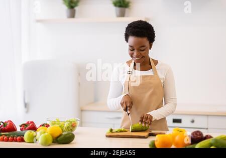 Cheerful Housewife Nero cucina taglio verdure preparazione cena in cucina Foto Stock