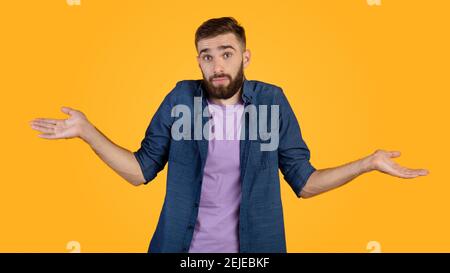 Non lo so. Bel ragazzo caucasico che si infrange le spalle, sentendosi perplesso o incerto su sfondo arancione studio Foto Stock