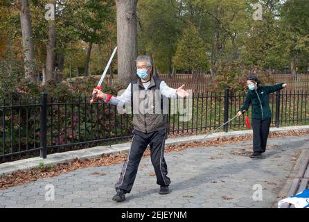 Un uomo e una donna asiatici americani pratica Tai Chi con spade prima di una classe. In un parco a Flushing, Queens, New York City. Foto Stock