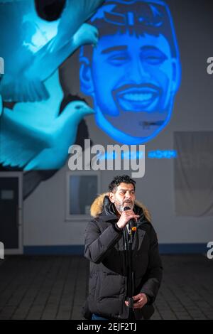 19 febbraio 2021, Hessen, Bruchköbel: Cetin Gültekin, fratello della vittima gökhan Gültekin, parla in memoria delle vittime durante la cerimonia commemorativa. Di fronte a un bar di narghilè a Bruchköbel, vicino Hanau, un gruppo di vittime si è riunito per commemorare l'omicidio razzista nell'anniversario dell'attacco di Hanau, con un graffiti e un'installazione leggera che proiettano le facce di coloro che sono stati uccisi sulla parete esterna del bar. Un estremista di destra aveva sparato nove persone ad Hanau il 19 febbraio 2020 per motivi razzisti. Successivamente, l'uomo aveva sparato sua madre e poi se stesso. L'atto ha causato hor in tutto il mondo Foto Stock