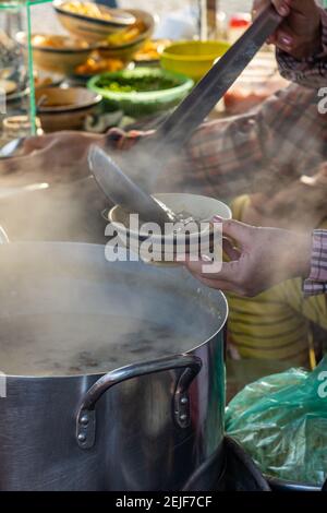 Donna che versa il porridge caldo nel recipiente al cibo di strada stallo Foto Stock