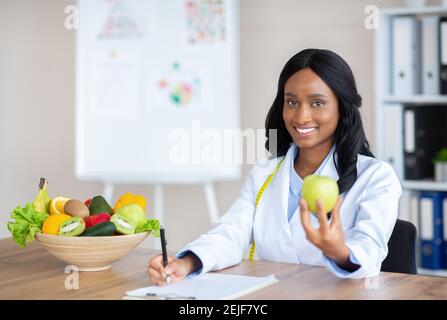 Ritratto di sorridente dietologo femminile che tiene la mela, raccomandando cibo fresco in clinica, copy space Foto Stock