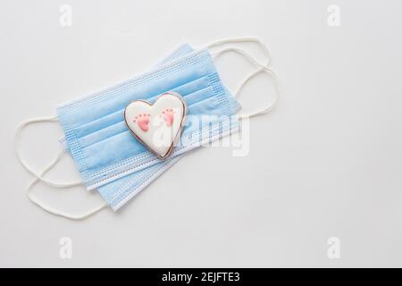 Maschera medica monouso e due cuori. Cuore con footprint del bambino. Parto nella pandemia del coronavirus Foto Stock
