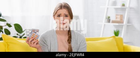 Donna triste con allergia che tiene vesciche con pillole e guardando la macchina fotografica una casa, banner Foto Stock