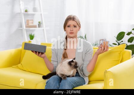 Donna dispiaciuta con pillole di contenimento allergico e scatola con tovagliolo vicino siamese cat Foto Stock