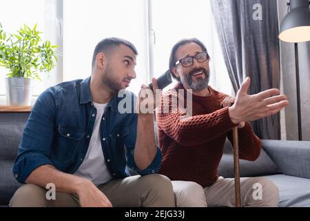 uomo dispiaciuto che punta con la mano mentre guardava la tv vicino al figlio tenere il telecomando Foto Stock