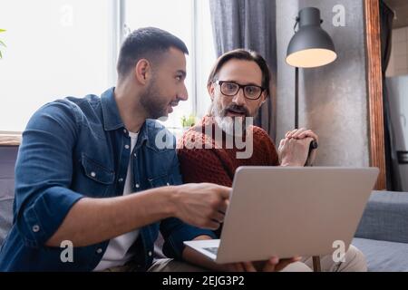 giovane uomo ispanico che punta al laptop vicino stupito padre Foto Stock