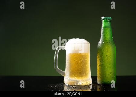 Tazza di birra e bottiglia su sfondo verde con copyspace. Foto Stock