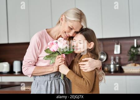 Mamma felice che riceve i fiori da una figlia di bambino teen il giorno delle madri. Foto Stock