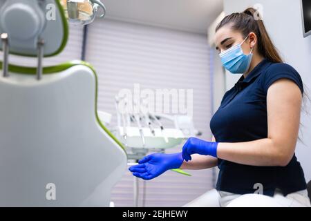 Il medico dentista in maschera mette i guanti sulle mani. Concetto di igiene medica Foto Stock