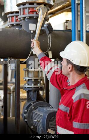 Tema del settore energetico: Un tecnico con tute rosse e casco bianco controlla i parametri di riscaldamento sui termometri. Manutenzione e ispezione. Foto Stock