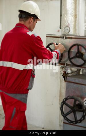 Tema del settore energetico: Un tecnico con tute rosse e casco bianco controlla i parametri di riscaldamento sui termometri. Manutenzione e ispezione. Foto Stock