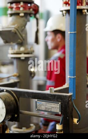 Tema del settore energetico: Un tecnico con tute rosse e casco bianco controlla i parametri di riscaldamento sui termometri. Manutenzione e ispezione. Foto Stock