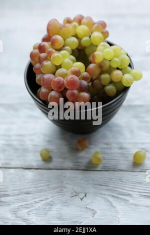 Uva verde rossa colorata in una ciotola nera su un tavolo di legno grigio, vista dall'alto. Foto Stock