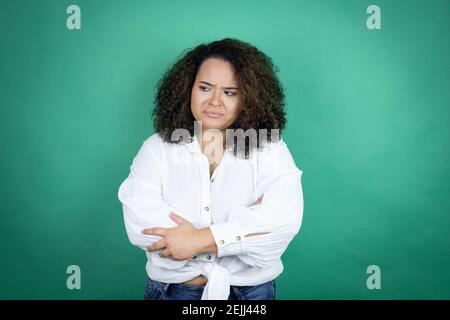 Giovane afroamericana ragazza con camicia bianca su sfondo verde pensare stanco e annoiato con le braccia incrociate Foto Stock