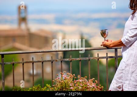 Vista ravvicinata della donna in abito bianco che tiene il bicchiere di vino d'argento contro il paesaggio sfocato. Vacanze estive in Toscana. Montalcino, Italia. Foto Stock