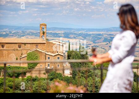 Vacanze in Toscana. Donna di mezza età con capelli lunghi e un abito bianco guarda il paesaggio della Toscana dalla terrazza di una casa medievale, enj Foto Stock