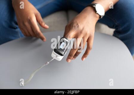 Uomo con pulsossimetro a portata di mano che misura la saturazione di ossigeno in ambienti interni Foto Stock