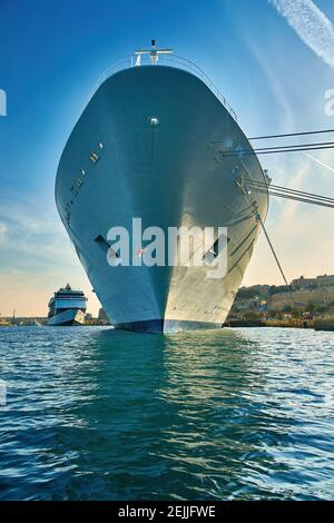 Vista frontale su un transatlantico ormeggiato nel porto dell'antica Valletta. Vista dalla superficie dell'acqua sul naso di un'enorme nave bianca contro il cielo blu. Foto Stock