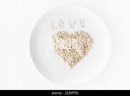 Cuore di farinata d'avena su un piatto bianco su sfondo bianco. Iscrizione Amore da fiocchi. Spazio per il testo. Foto Stock