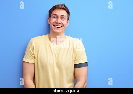 positivo uomo in t-shirt casual si alza in contemplazione, sorridente. isolato su sfondo blu studio. stile di vita, persone, emozioni umane concetto Foto Stock