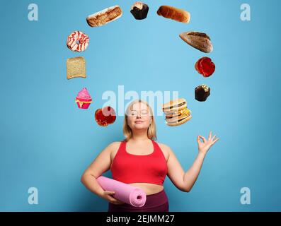 Fat ragazza fa palestra a casa, ma pensa sempre a mangiare. Sfondo ciano Foto Stock