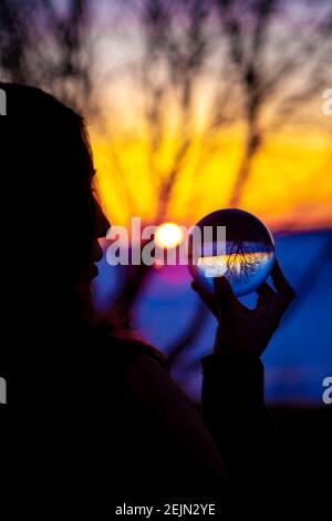 Ragazza nativa che guarda in Crystal Ball sulla riva di Un lago ghiacciato con un tramonto magico Foto Stock