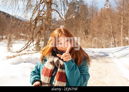 Cute Girl nei vestiti invernali punta Finger flirtatiously con la neve Montagne coperte in background nelle Alpi europee in Germania Austria Svizzera Foto Stock